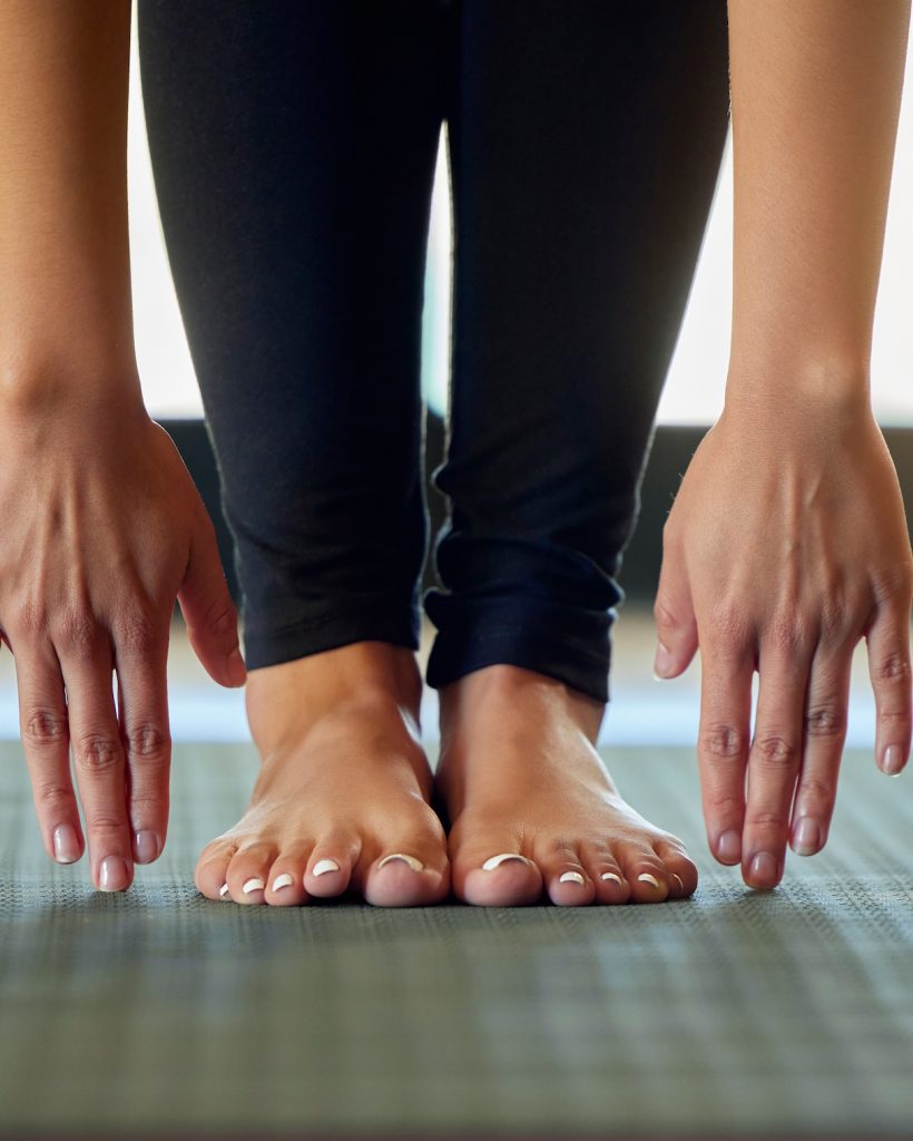 Hands, feet and woman stretching on yoga mat for exercise, cardio and flexibility warm up in her home. Barefoot, hand and girl stretch for meditation, training for pilates workout in a living room.