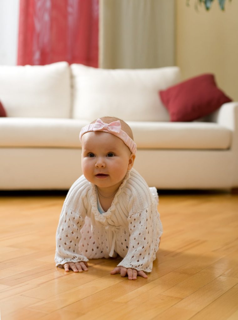 Happy eight month old baby girl crawling on a hardwood floor in living room